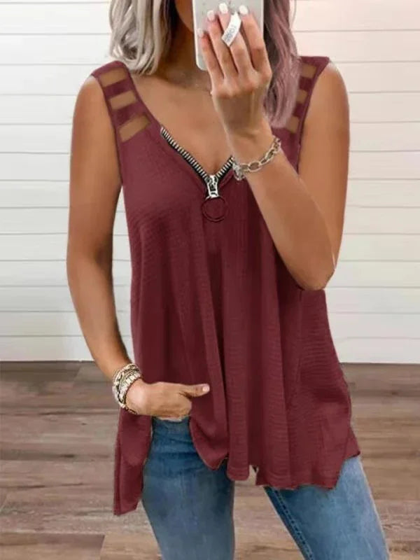 Woman wearing sleeveless burgundy top with zipper and mesh strap detail paired with blue jeans