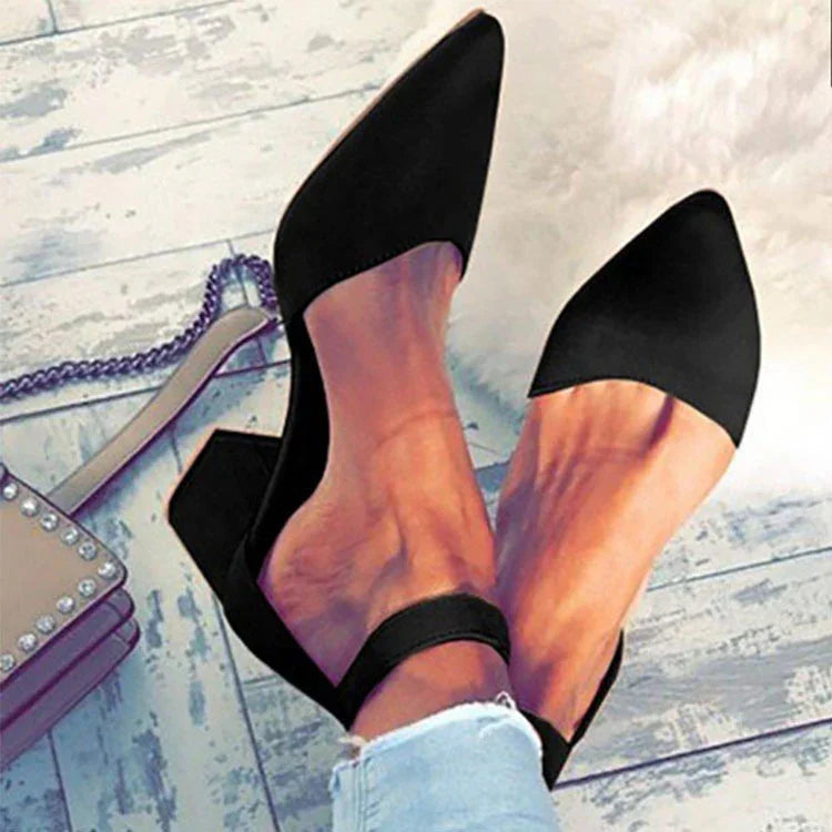 Woman wearing black pointed toe block heel shoes with ankle strap on white wooden floor