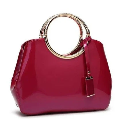 Glossy red handbag with gold circular handles and attached tag on white background