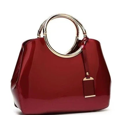 Glossy red handbag with gold metal round handles and a matching tag accessory