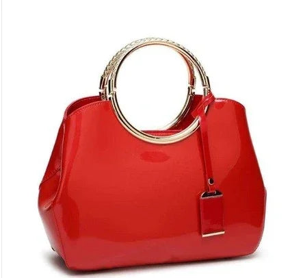 Shiny red handbag with large gold circular handles and a hanging leather tag