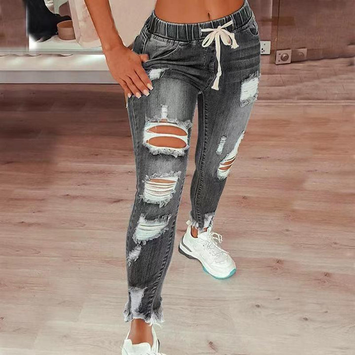 Woman wearing distressed black denim jogger jeans with drawstring waist and white sneakers on wooden floor
