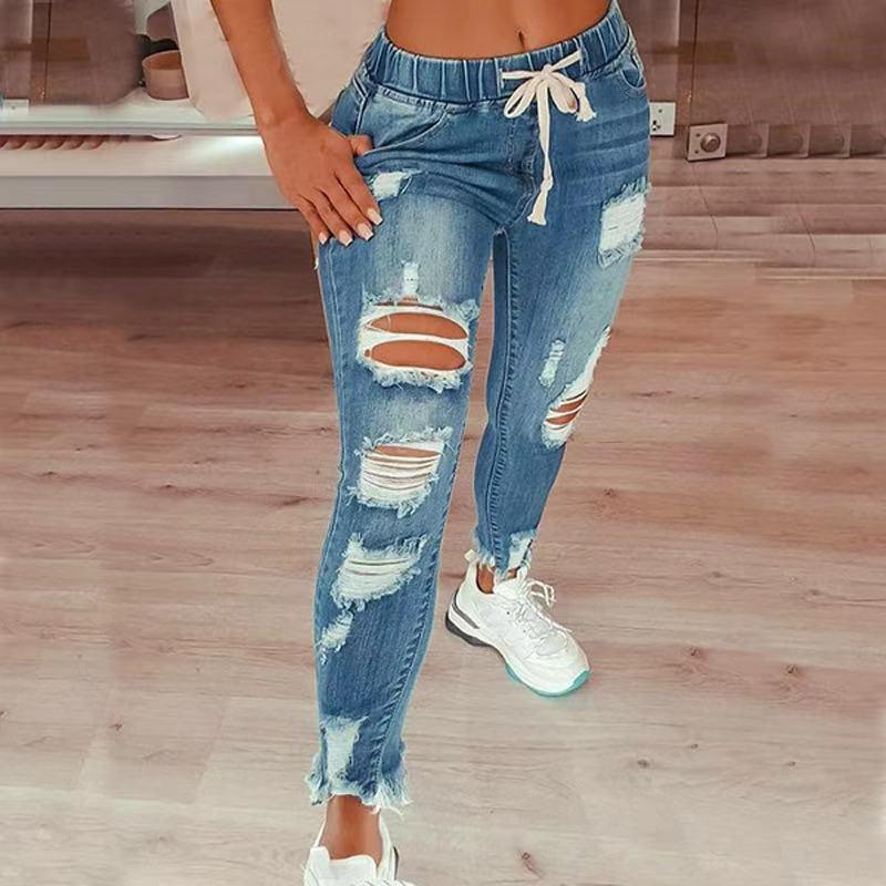 Woman wearing blue distressed denim jogger jeans with drawstring waist and white sneakers indoors