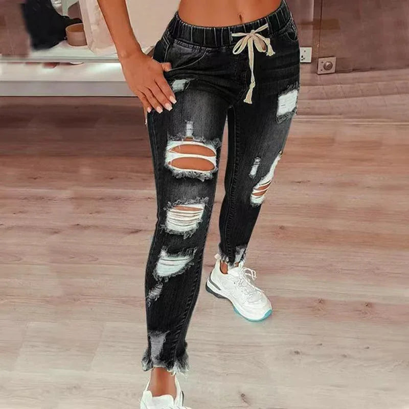 Woman wearing black distressed ripped jeans with drawstring waist and white sneakers on wooden floor