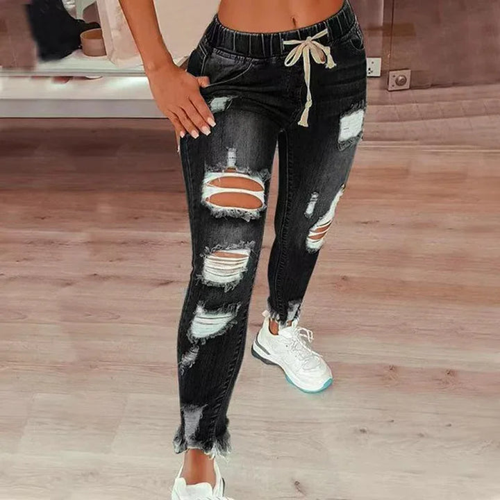 Woman wearing black distressed ripped jeans with drawstring waist and white sneakers on wooden floor
