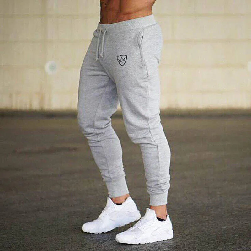 Man wearing gray slim-fit jogger pants with logo and white athletic sneakers on indoor floor