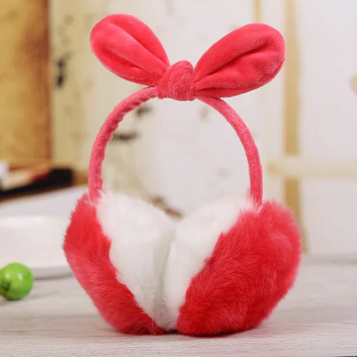 Red and white fluffy earmuffs with a red bow headband on a wooden surface