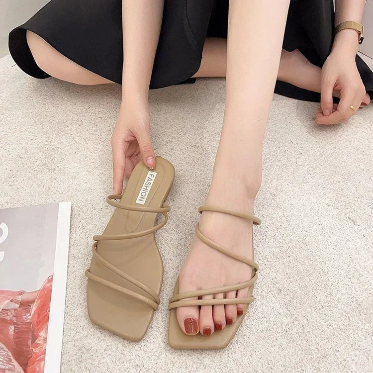 Close-up of woman wearing beige strappy sandals with square toes on beige carpet