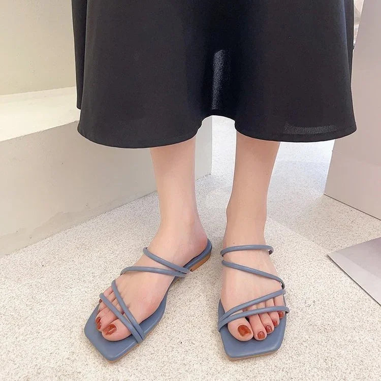 Feet wearing stylish blue strappy square-toe sandals with red nail polish on beige floor