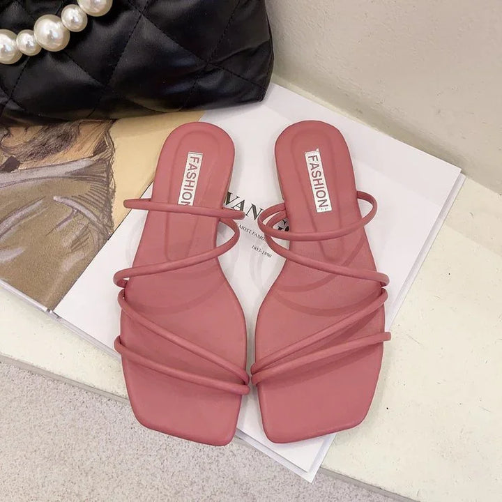 Pink strappy flat sandals with square toes on magazine near black quilted bag with pearl handle