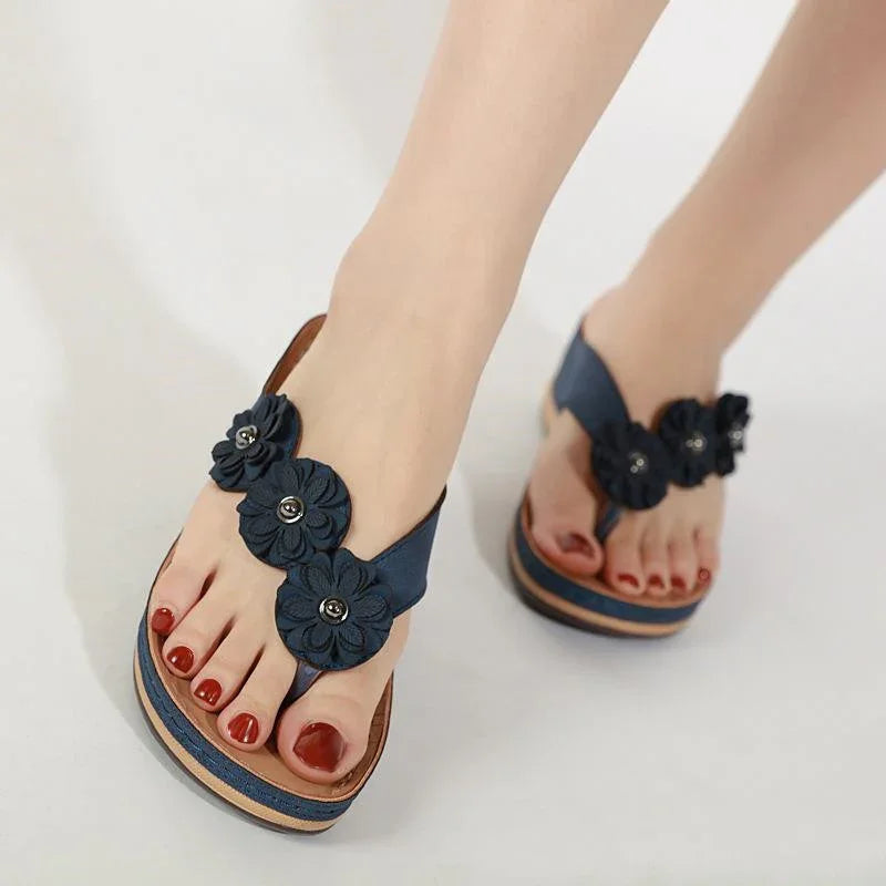 Woman wearing navy blue floral thong sandals with red polished toenails on a white background