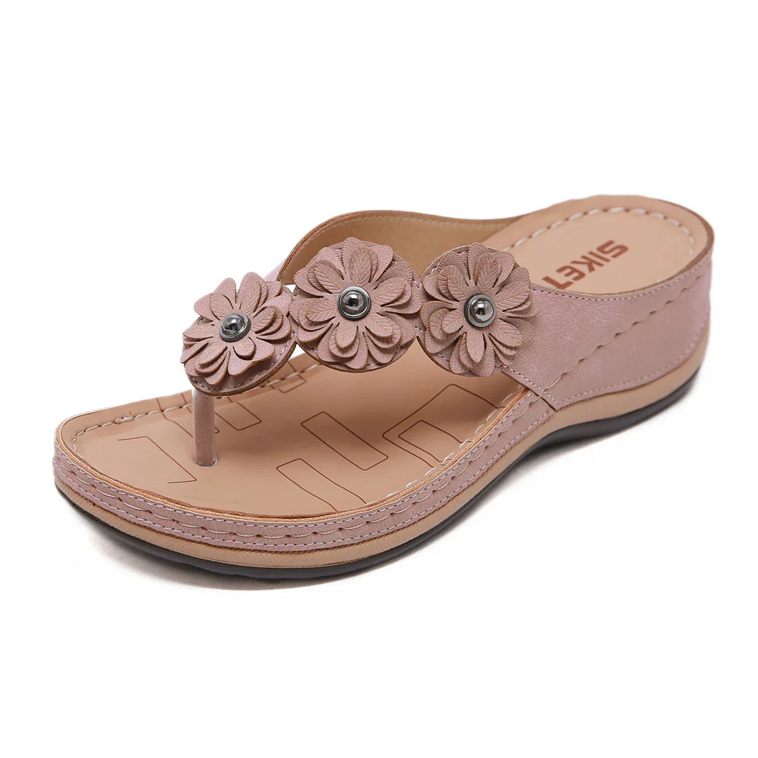 Pink wedge sandal with three floral decorations and ankle strap on a white background