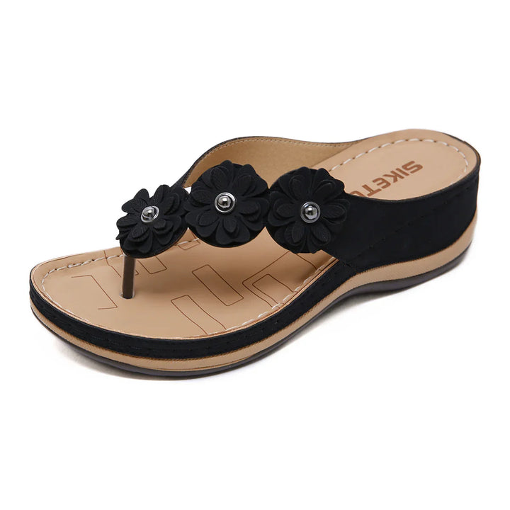 Black women's wedge sandal with three decorative black flower accents and beige sole