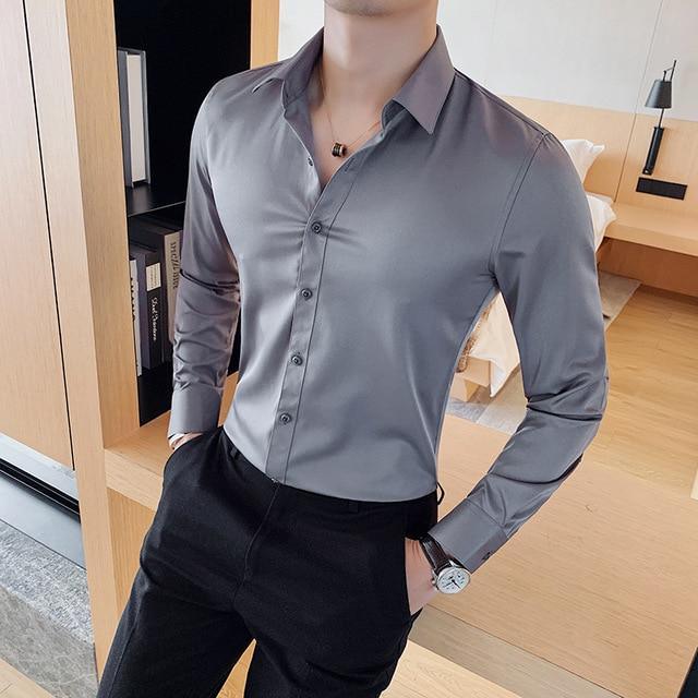 man wearing fitted gray satin dress shirt and black pants in modern bedroom setting