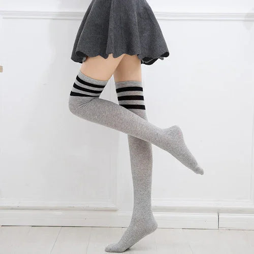 Person wearing gray thigh-high socks with black stripes and a charcoal gray skirt against a white wall