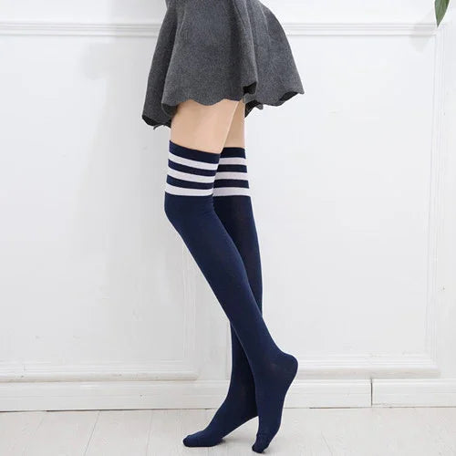 Long navy blue thigh-high socks with white stripes paired with a grey skirt against white wall