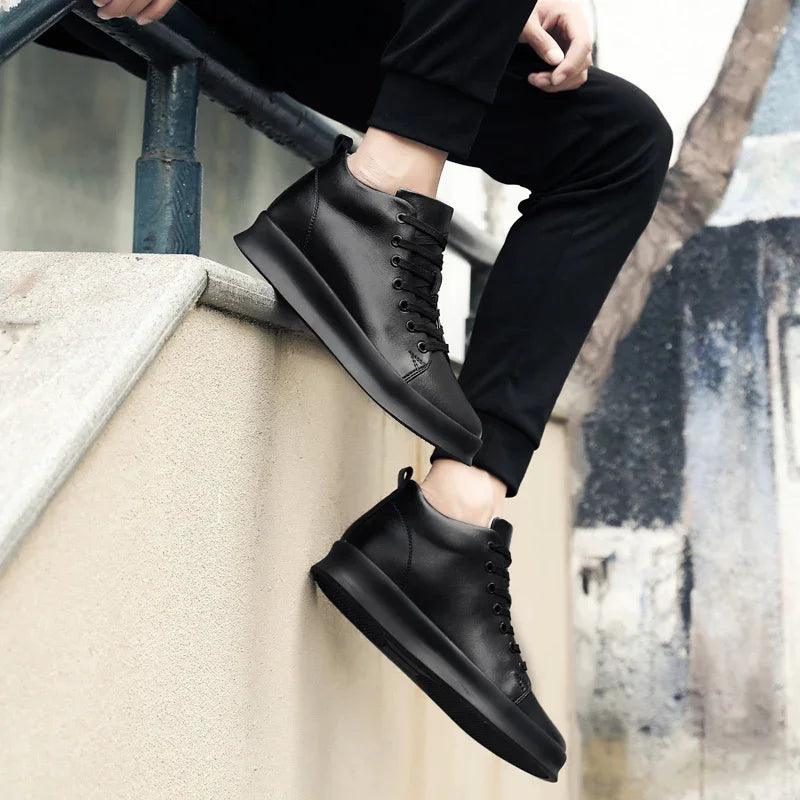 Person wearing black leather high-top sneakers sitting on a concrete ledge with urban background