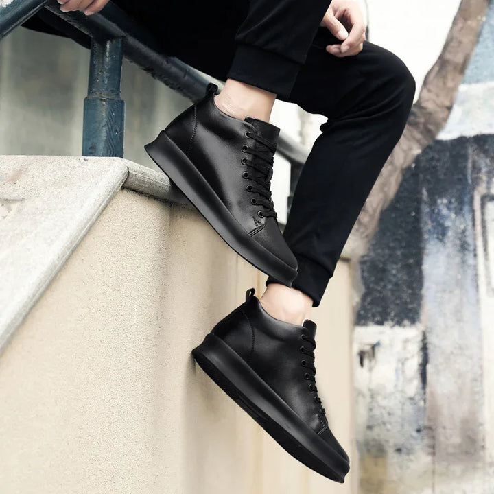 Person wearing black leather high-top sneakers sitting on a concrete ledge with urban background