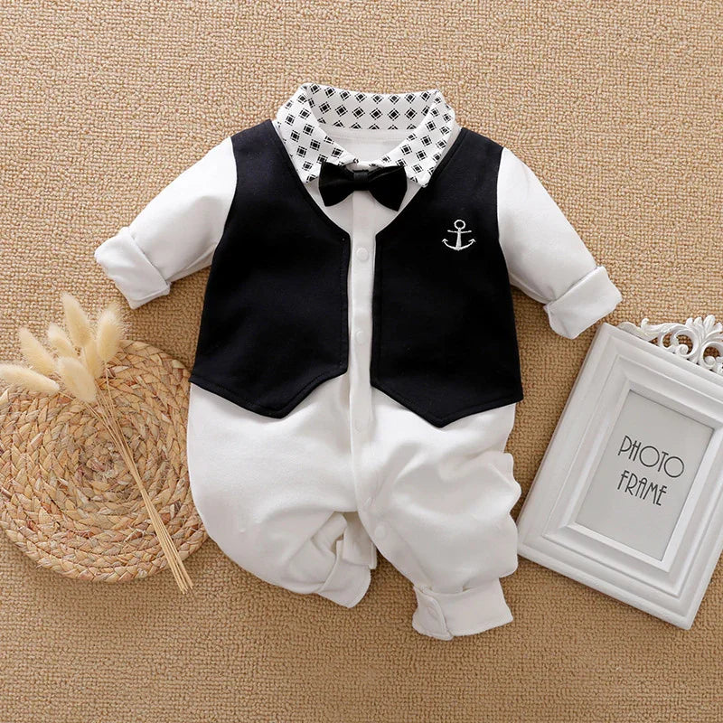 baby boy white romper with black vest, patterned collar, black bow tie, and anchor detail on beige background