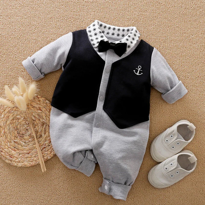 Gray baby romper with black vest, bow tie, printed collar, and white baby shoes on beige mat
