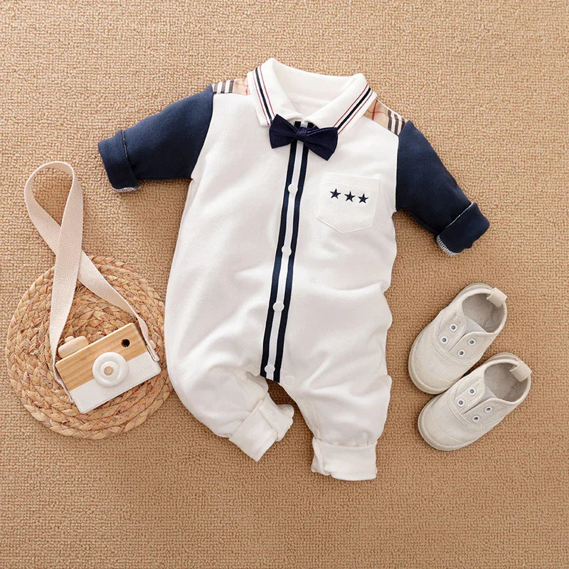 Stylish baby boy romper with navy sleeves, bow tie, and star pocket detail, paired with white baby shoes and toy camera