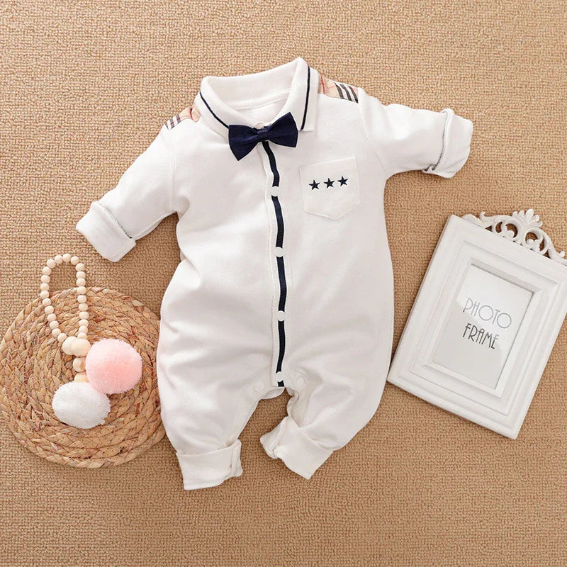 White baby romper with navy bow tie and star pocket detail on textured beige surface