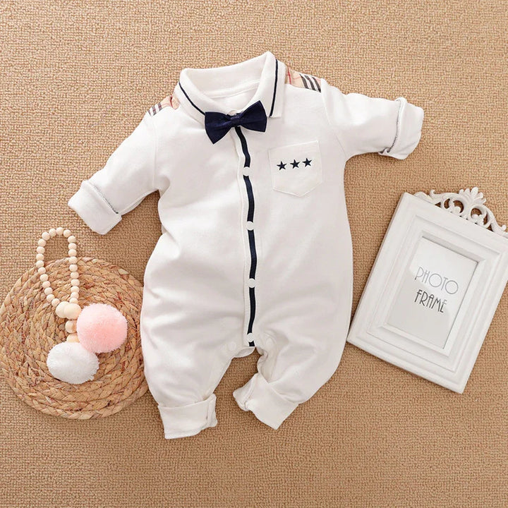White baby romper with navy bow tie and star pocket detail on textured beige surface