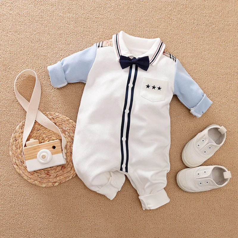 Baby boy formal romper with blue sleeves, navy bow tie, and white shoes on beige carpet