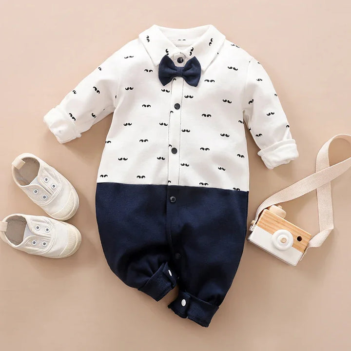 Infant white and navy blue one-piece outfit with bow tie and eye print pattern, paired with white baby shoes and toy camera