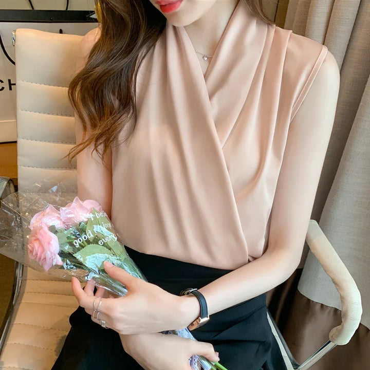 Woman wearing sleeveless beige blouse holding pink roses while sitting on cream office chair