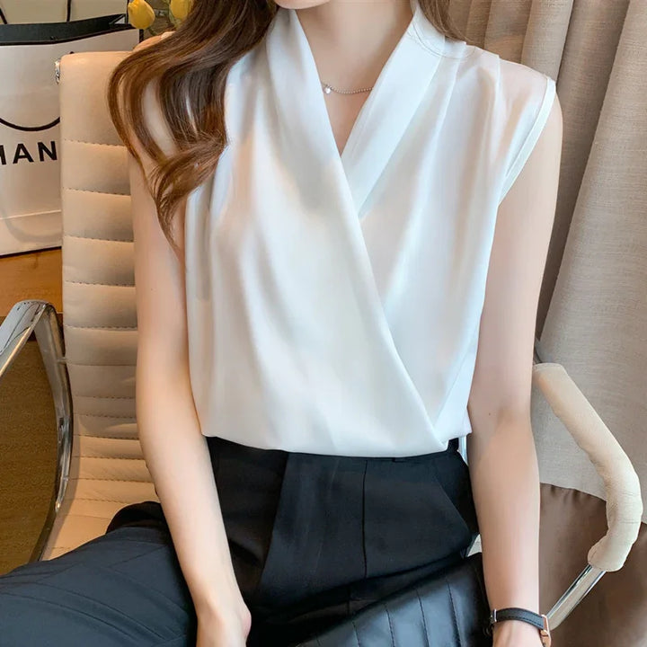 Woman wearing sleeveless white wrap blouse and black high-waist pants sitting on modern office chair