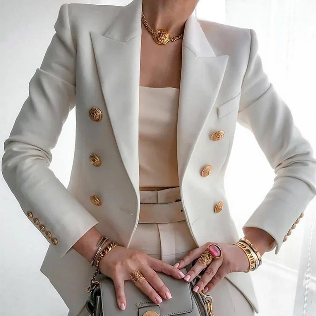 Woman in white double-breasted blazer with gold buttons, beige top, and gold jewelry holding gray handbag