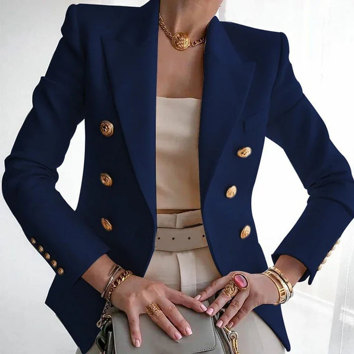 Woman wearing navy double-breasted blazer with gold buttons, beige top and pants, holding gray handbag