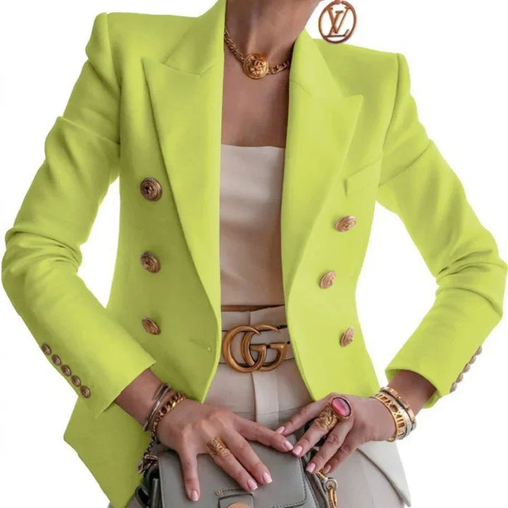 Woman wearing neon yellow blazer with gold buttons, beige top, Gucci belt, gold jewelry, and holding a gray handbag