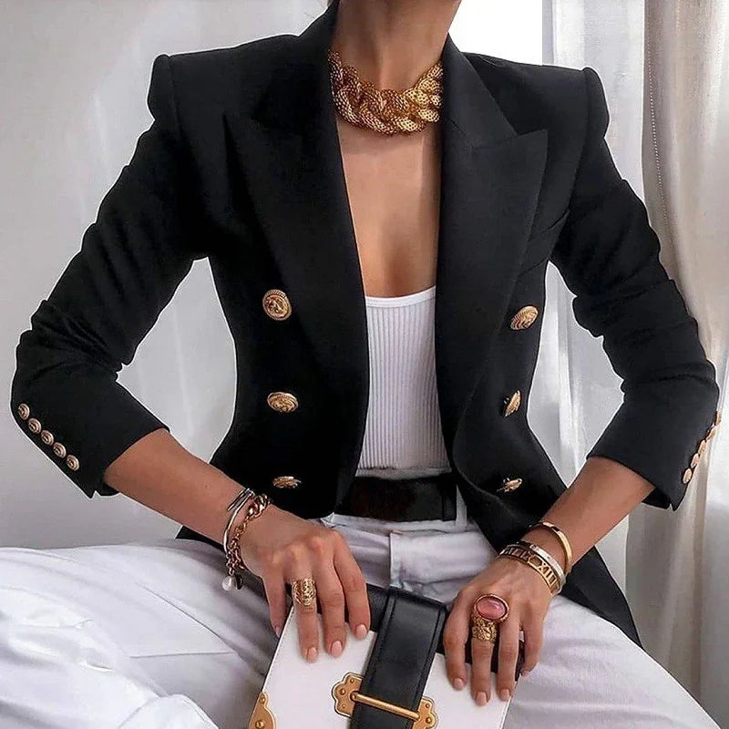 Fashionable woman wearing black double-breasted blazer with gold buttons, white top, white pants, gold jewelry, and holding black and white purse
