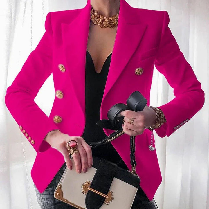 Woman wearing a bright pink blazer with gold buttons, black top, and gold jewelry holding a black and beige handbag