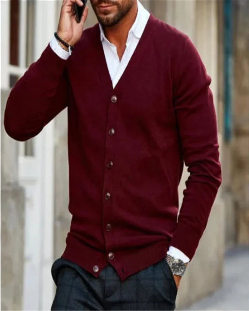 Man wearing a burgundy buttoned cardigan over white shirt, paired with dark plaid pants, urban background