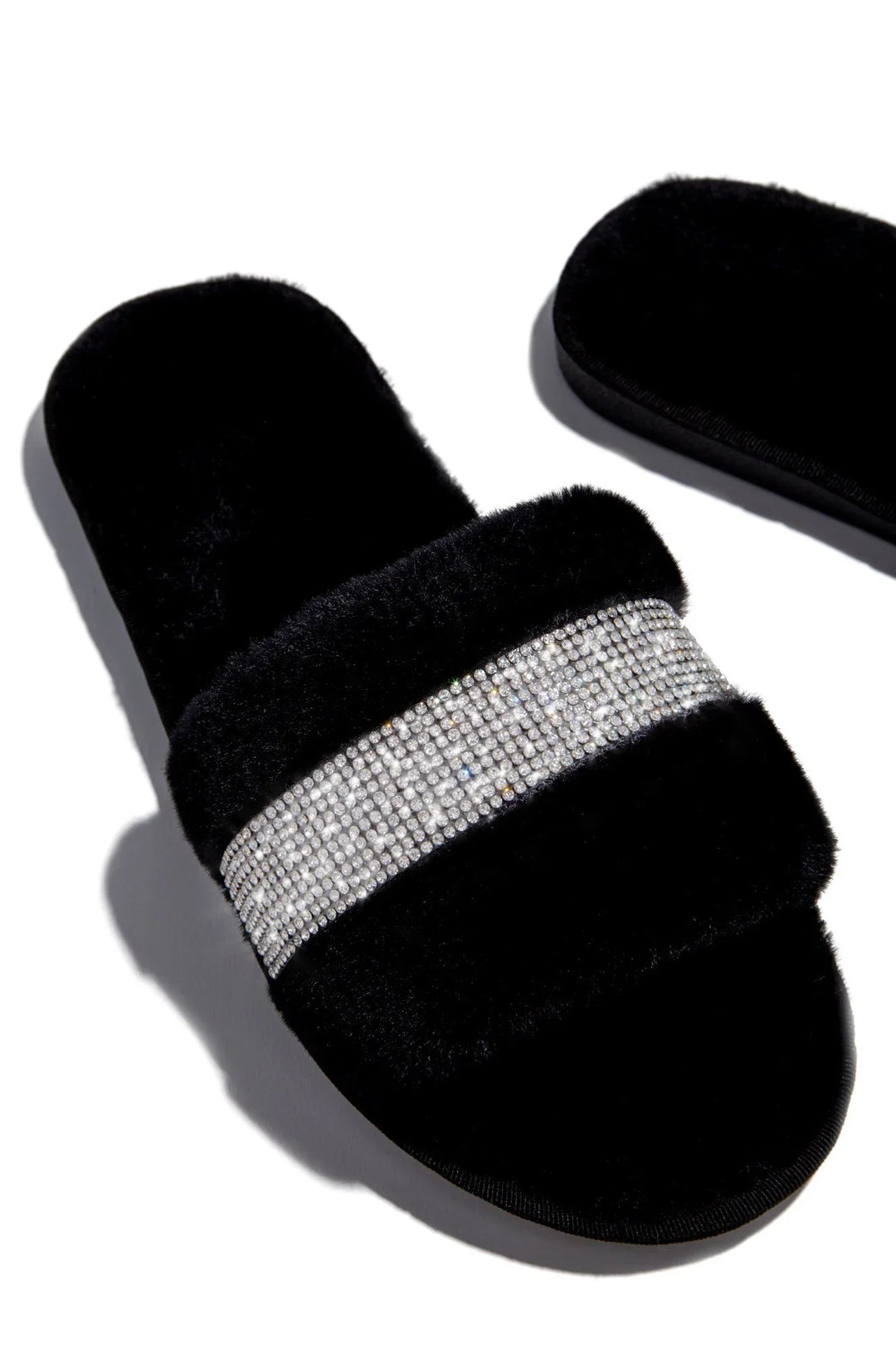 Black furry slide slippers with a sparkling rhinestone band on top, isolated on white background