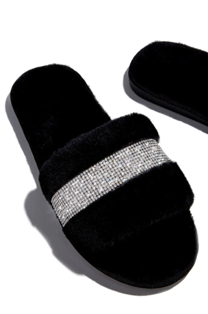 Black furry slide slippers with a sparkling rhinestone band on top, isolated on white background