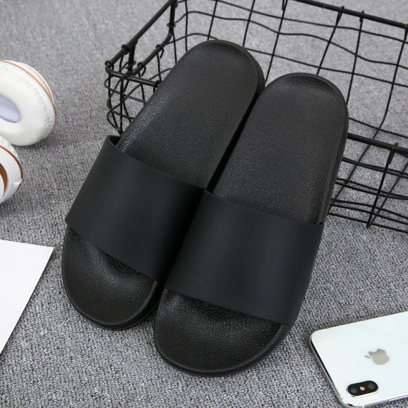 Pair of black slide sandals on gray carpet near a black wire basket and white smartphone