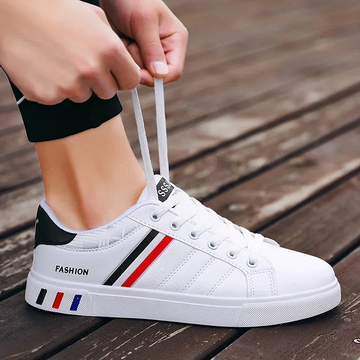 Close-up of white casual sneakers with red, black, and blue stripes being laced on wooden floor