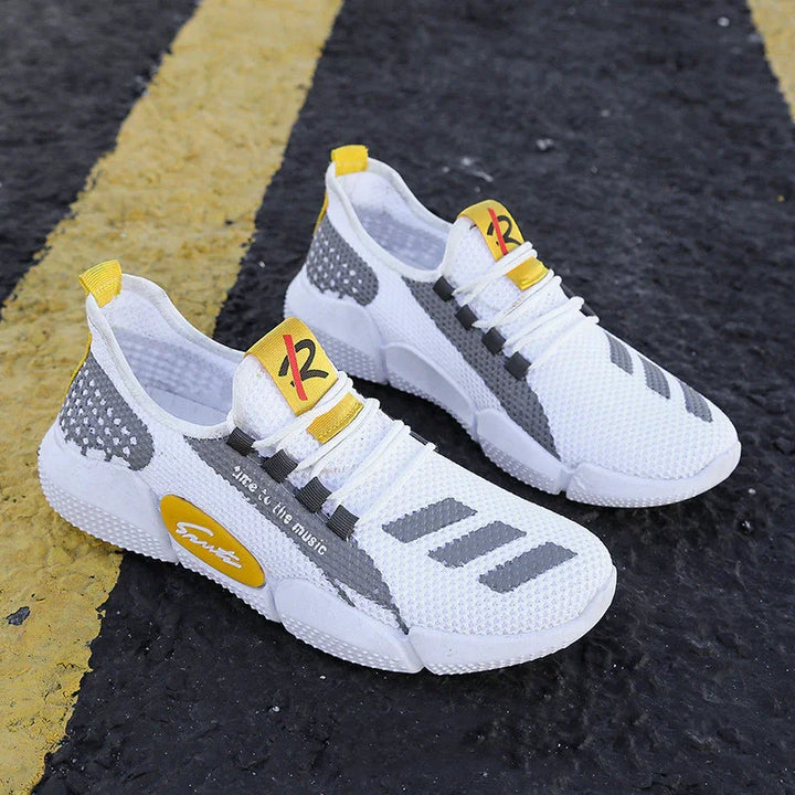 White and gray knitted sports shoes with yellow accents placed on black asphalt with yellow lines
