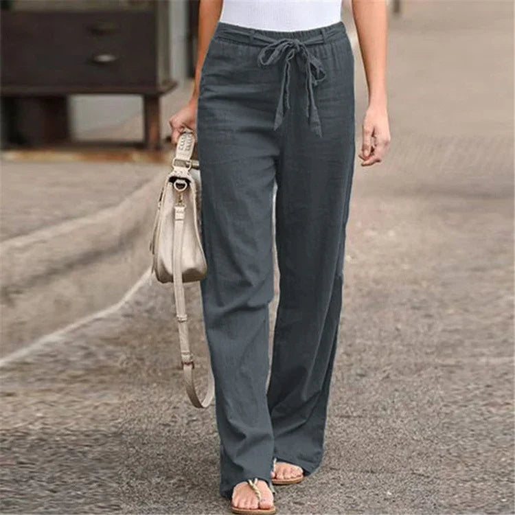 Woman wearing charcoal gray drawstring linen pants with beige handbag and sandals on street