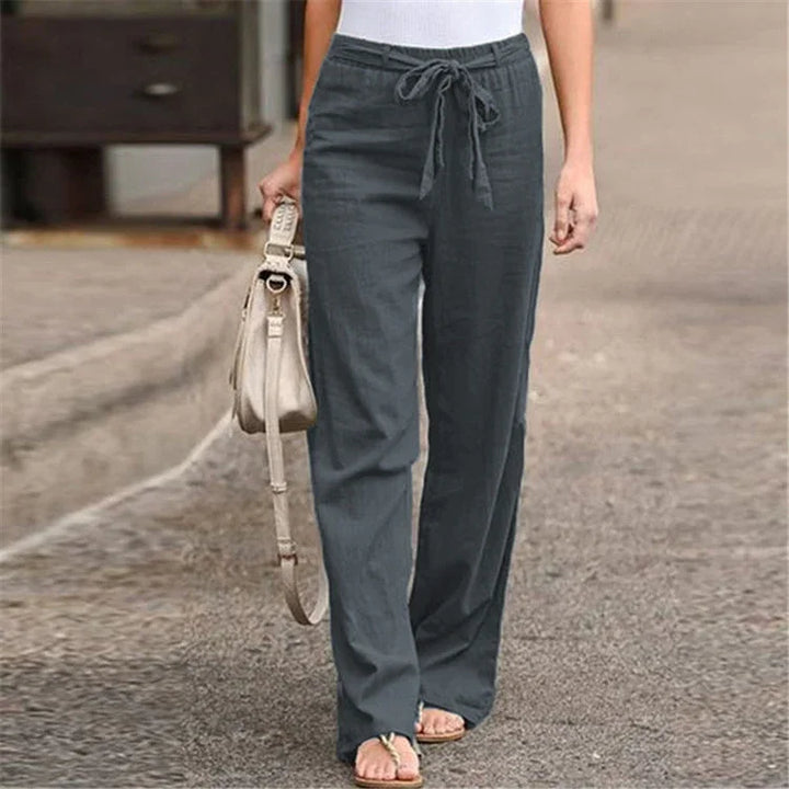 Woman wearing charcoal gray drawstring linen pants with beige handbag and sandals on street