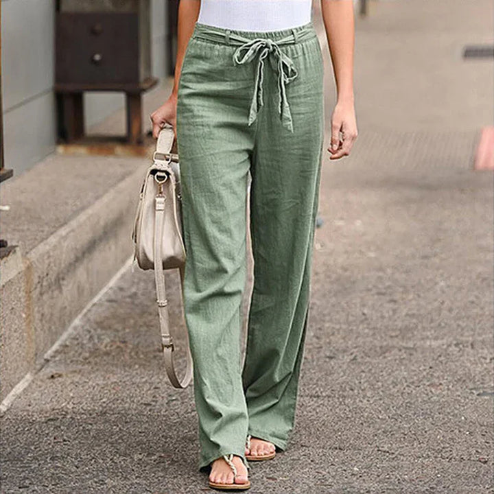 Woman wearing casual green linen pants with drawstring waist and white tank top, carrying beige bag