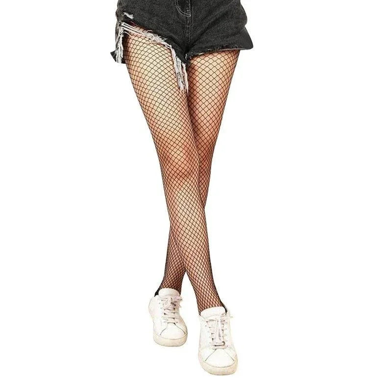 Woman wearing black ripped denim shorts, black fishnet tights, and white sneakers against white background