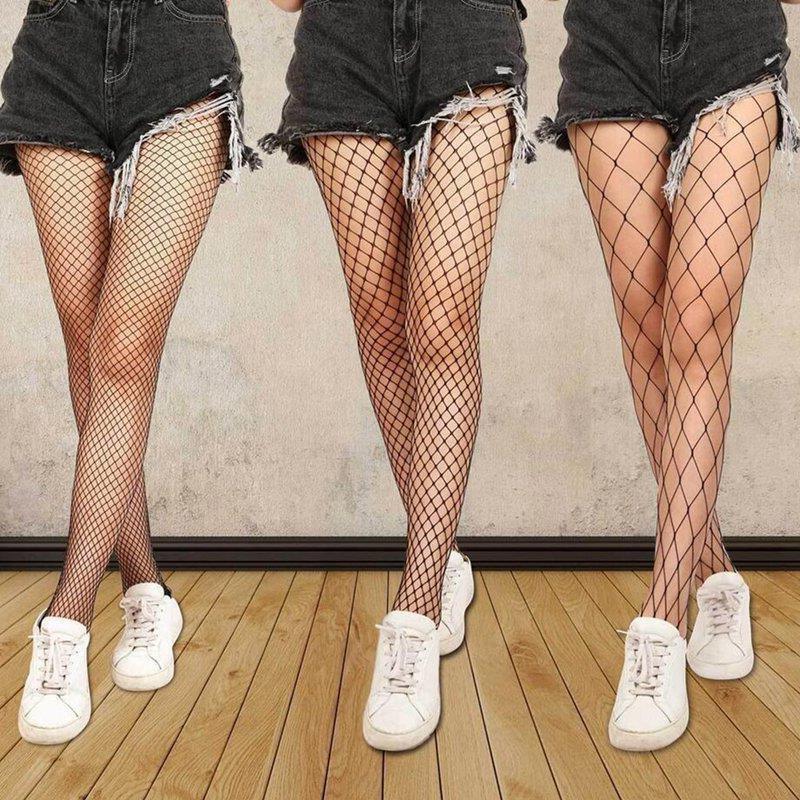 Three pairs of legs in black fishnet stockings and black distressed shorts with white sneakers on wooden floor