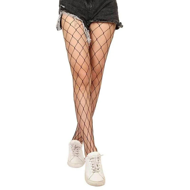 Legs wearing black fishnet tights paired with black denim shorts and white sneakers on white background