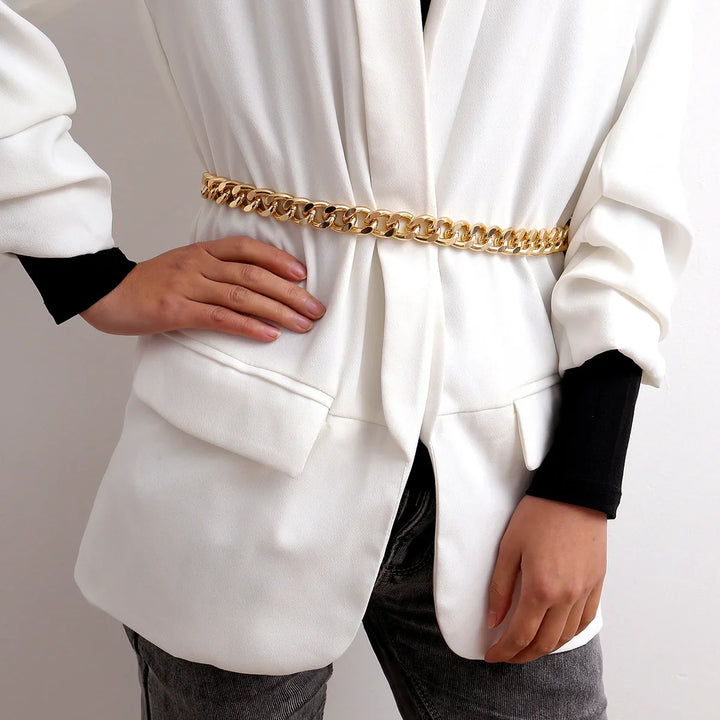 Woman wearing white blazer with gold chain belt and black inner sleeves posing with hand on waist