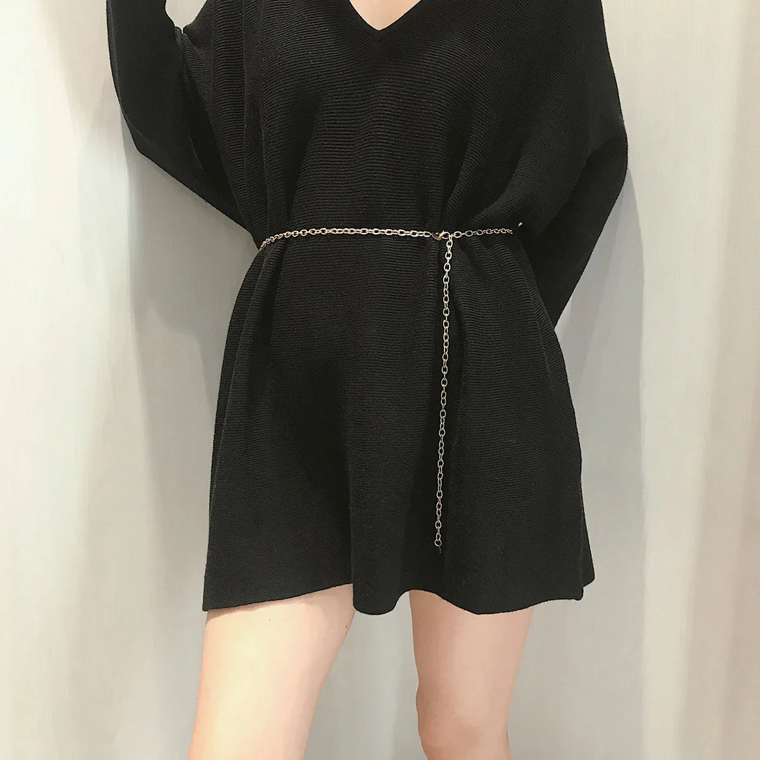 Woman wearing a black ribbed knit mini dress with a slim gold chain belt in a neutral indoor setting